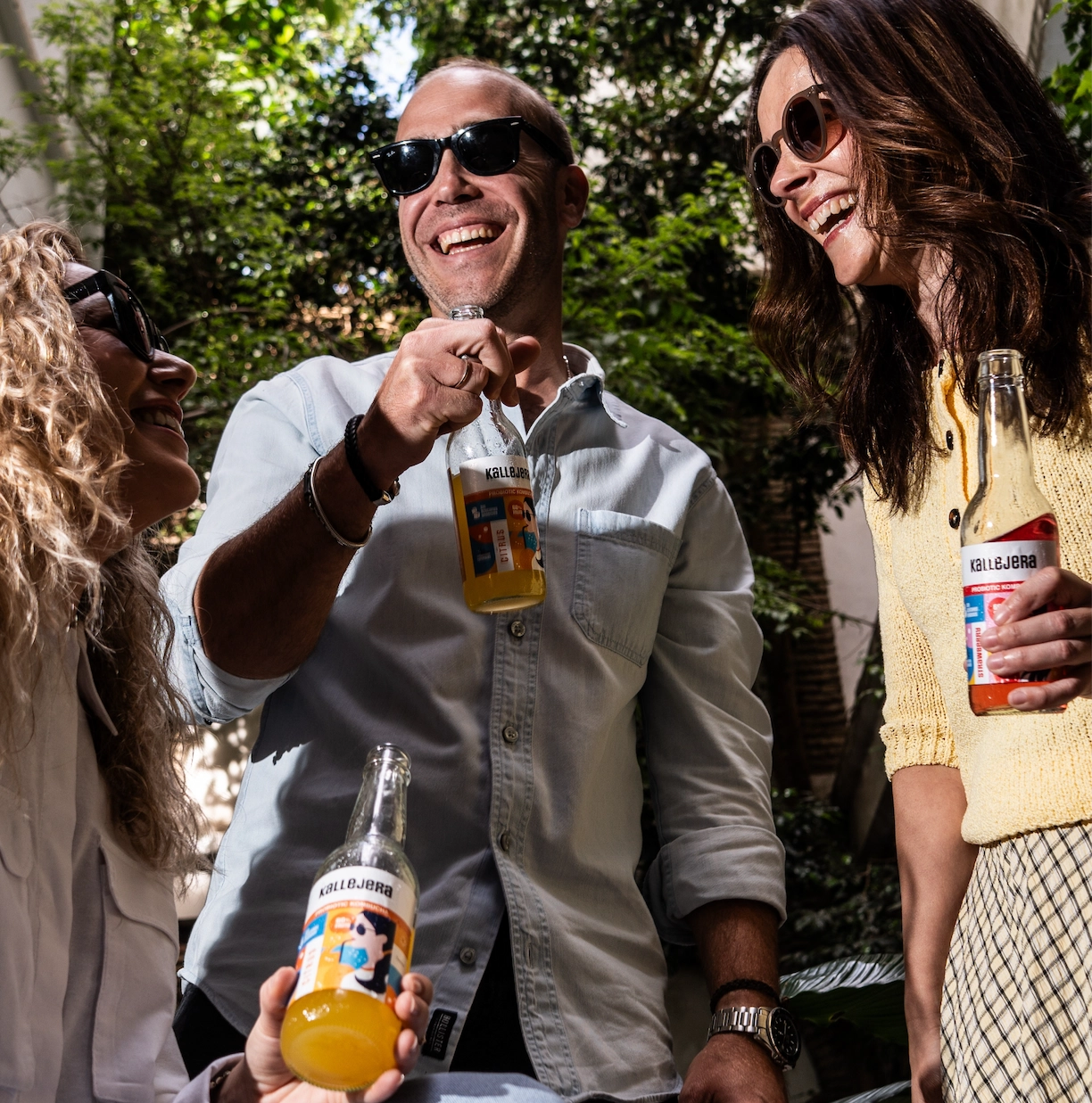 Tres amigos riendo con botellas de kombucha Kallejera.