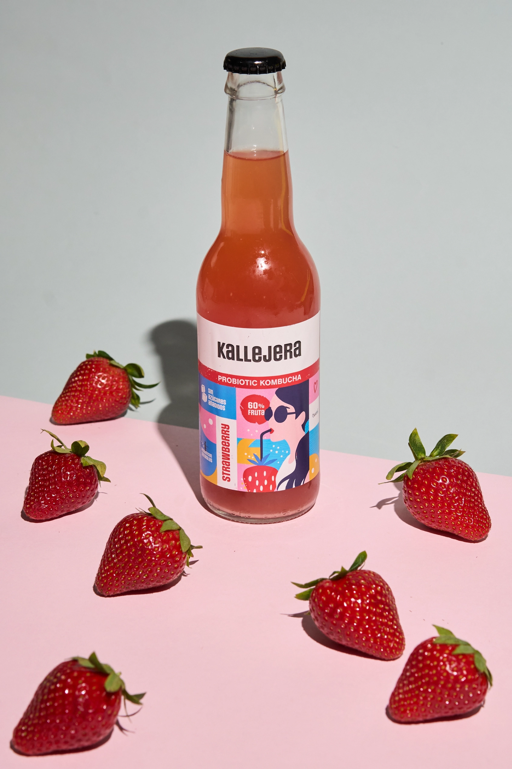 Botella de kombucha de fresa Kallejera rodeada de fresas naturales.