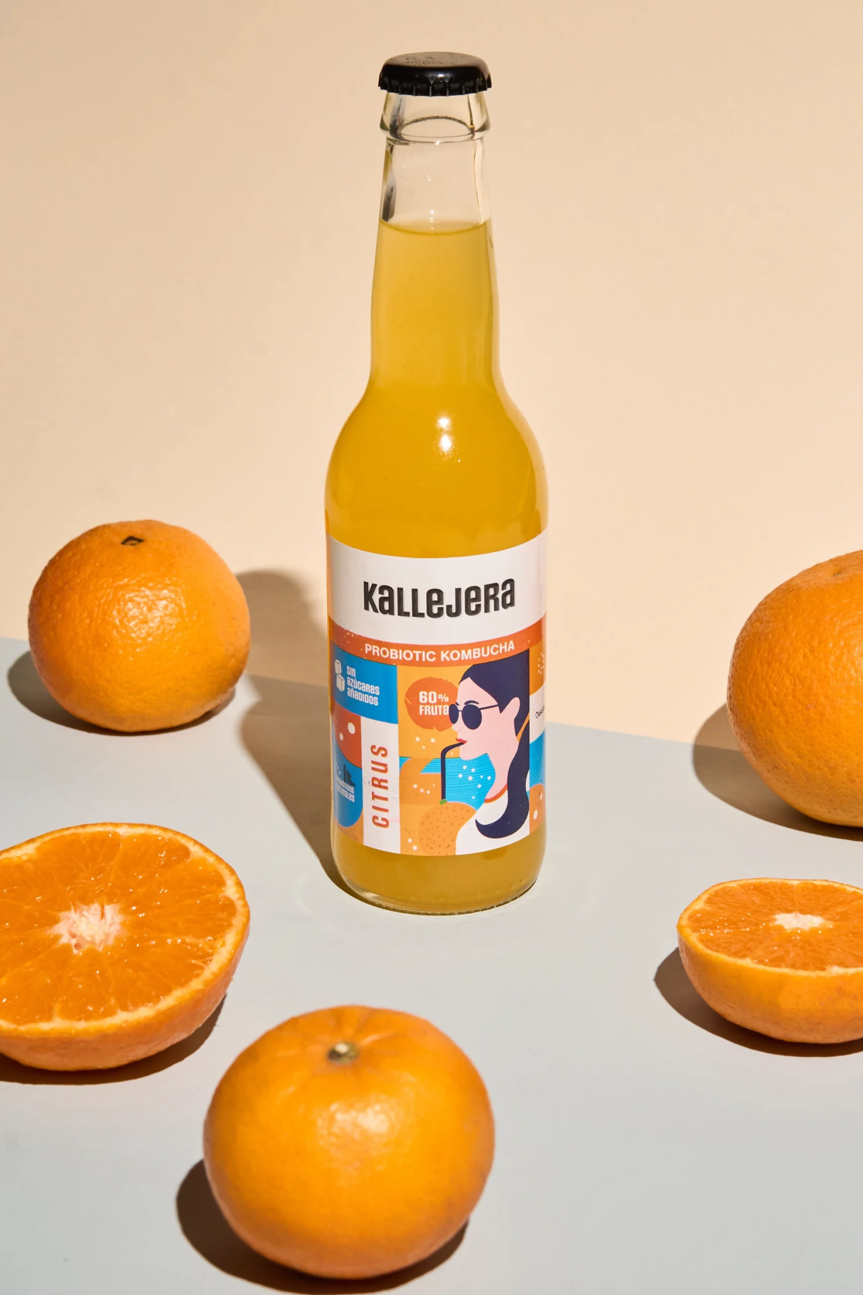 Botella de kombucha Kallejera cítrica rodeada de naranjas frescas.